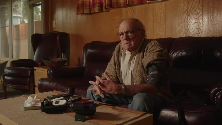 An older man with a blood pressure cuff on his arm while he sits on his couch looking nervous