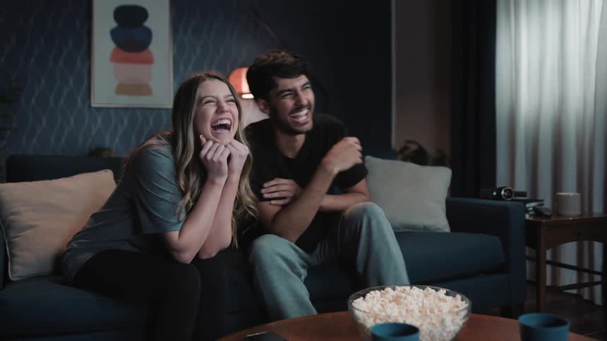 Young couple is sitting on the couch and eating some popcorn