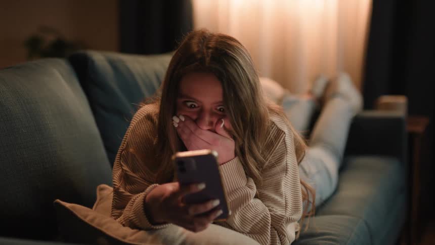 A young woman is laying on the couch and looking at her phone