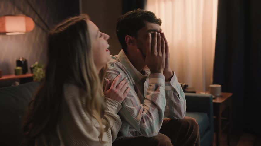 Man sitting with his date watching movies at home makes her laugh faking a reaction