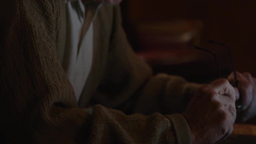 An up close of an older mans hands holding his glasses and then focusing on his face