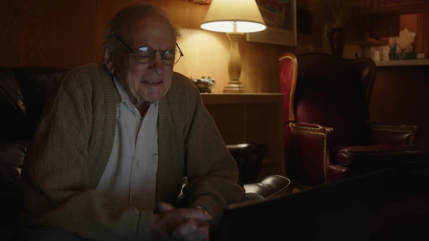 Happy excited elderly man sitting on a couch in the living room typing on a laptop