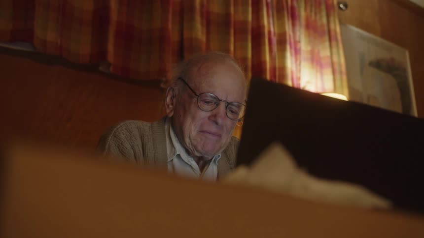 An older elderly man is sitting down and going on his laptop