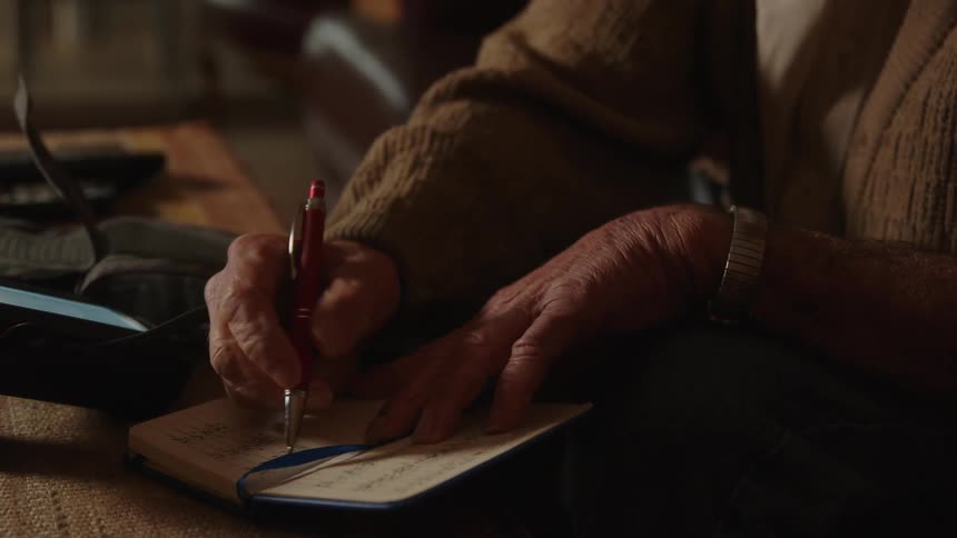 An old man makes notes in a notebook