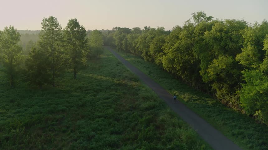 Person roller skates along road passing field and woods
