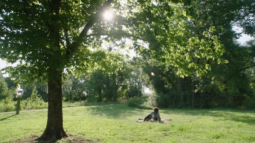 Young man sitting with his dog over the green grass on a park at morning