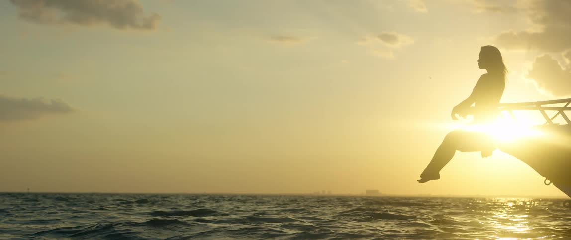 A woman suspended over the ocean at sunset