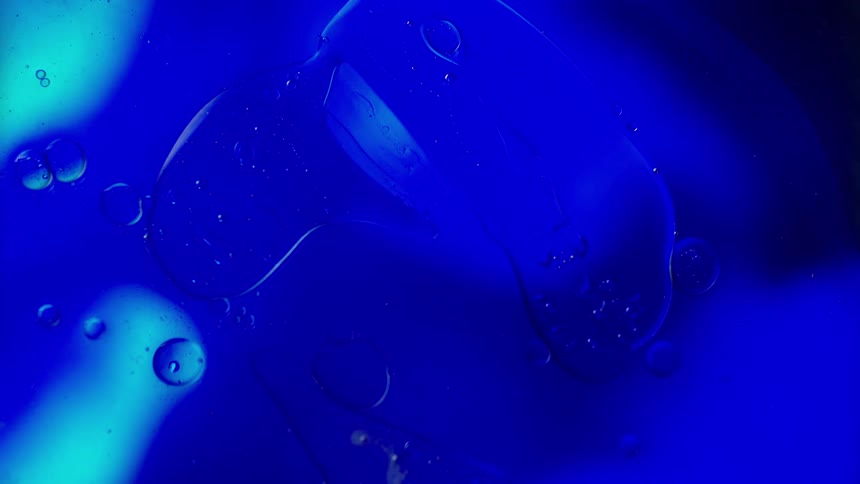 Water drops move across clear glass as blue light glow in the distance
