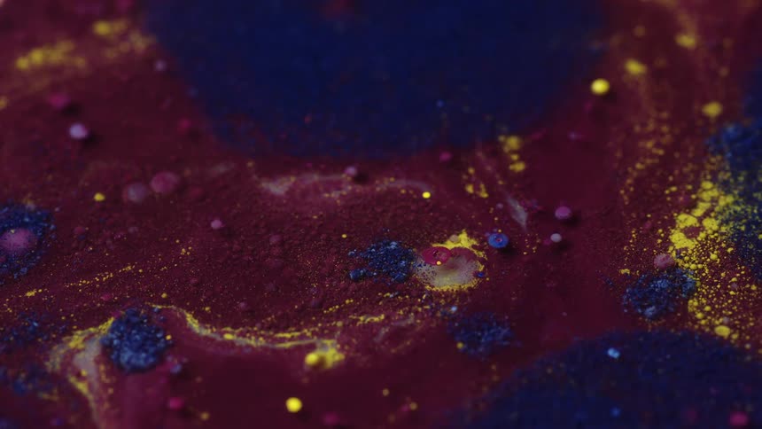 Small droplets of colorful liquid float atop another paintlike liquid