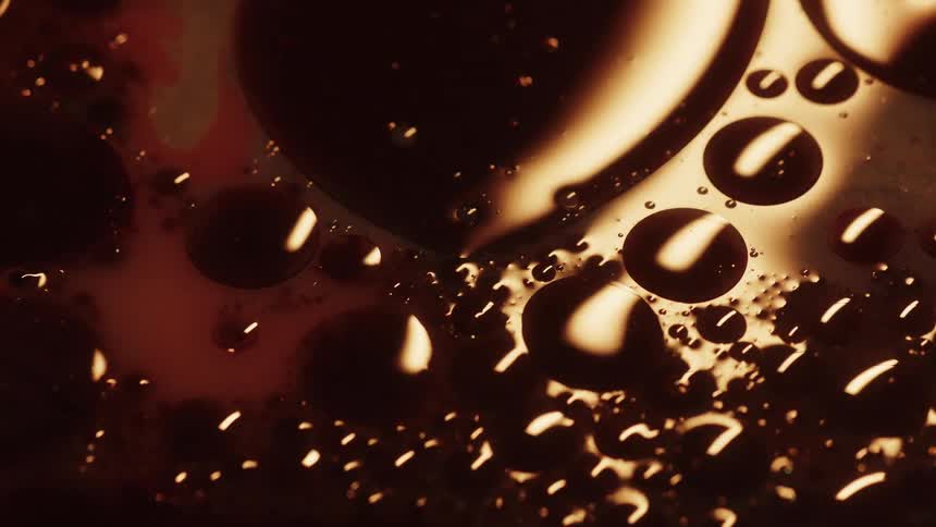 Light shines on shiny spheres as they move and float on liquid in the darkness