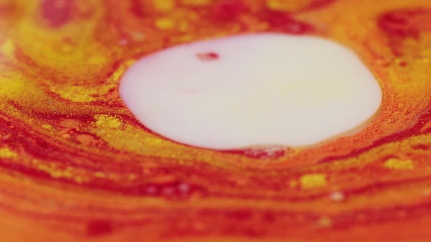 A white liquid rises up and spreads throughout a foamy orange liquid