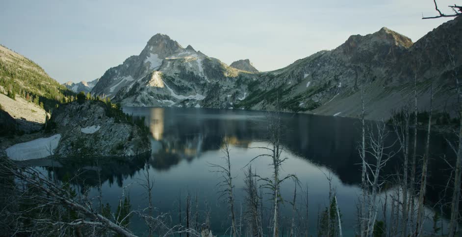 Calm surface of a lake surrounded by the snow covered slopes of a mountain range at morning