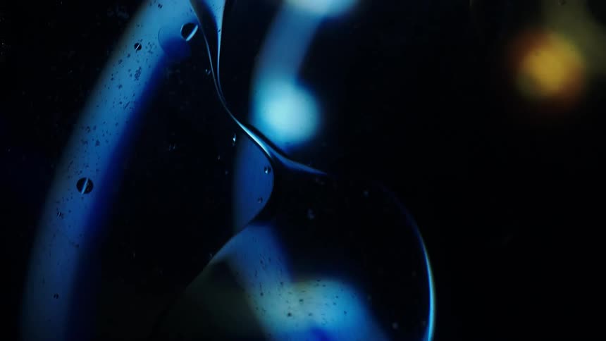 Colored lights glow in the distance as clear liquid drips and reflects the colors