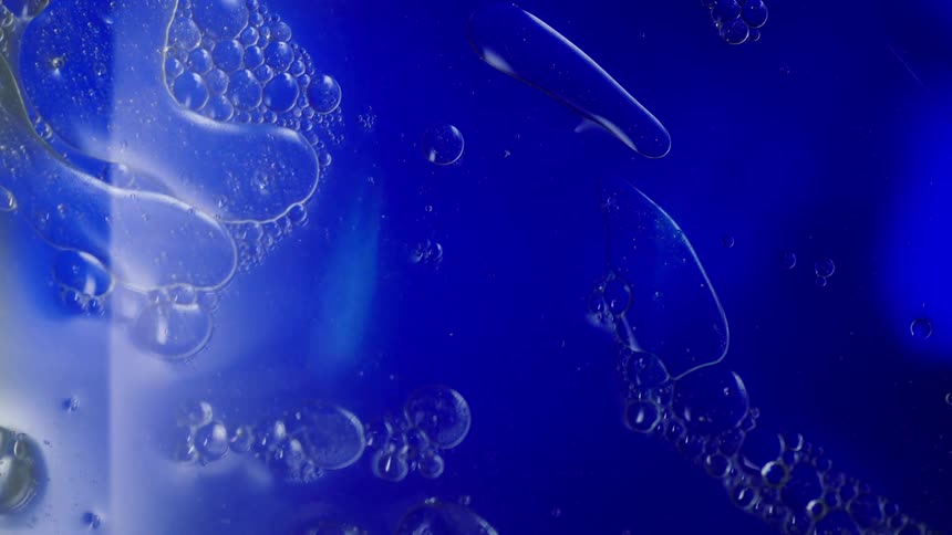 Abstract closeup of blue liquid oil and water mixture with bubbles and light and shadow moving across
