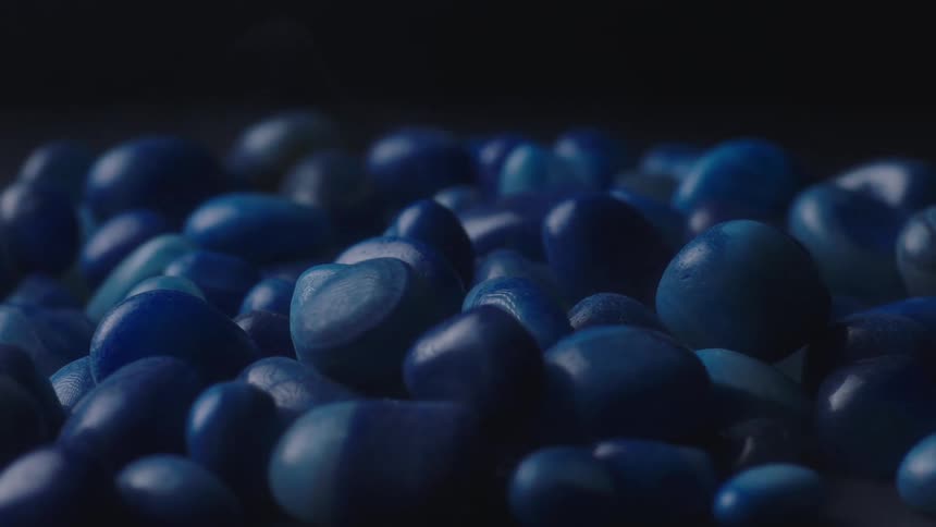 Orbiting close up of a bunch of blue pebbles piled up against a dark background