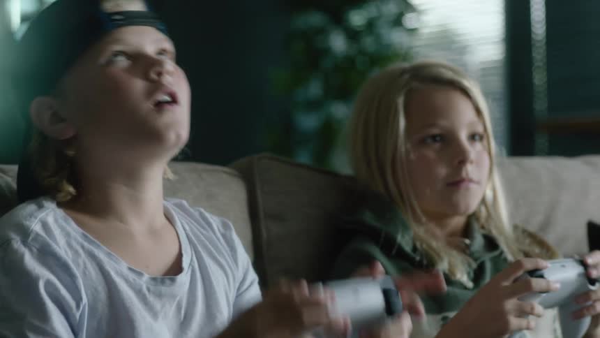 A young boy and girl sit on a couch while playing video games together
