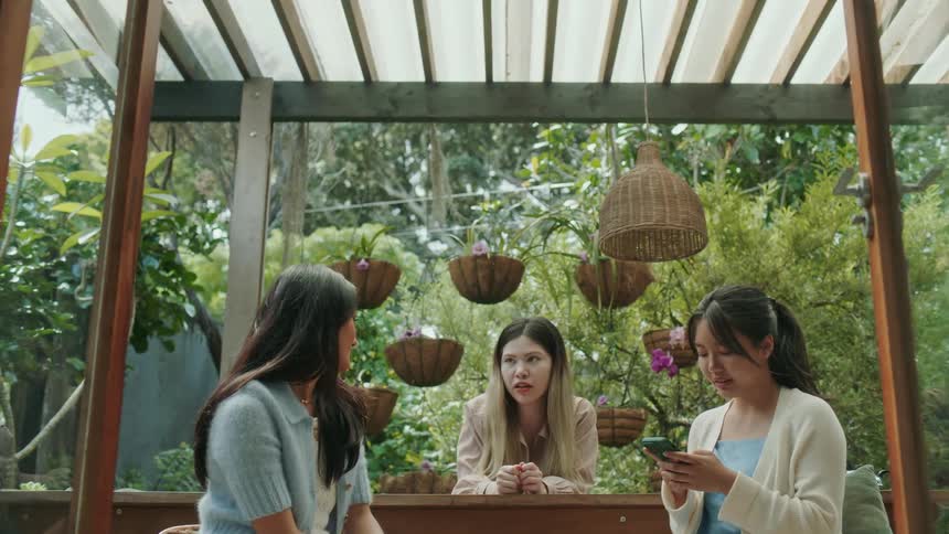 Three friends talk while one uses a cell phone