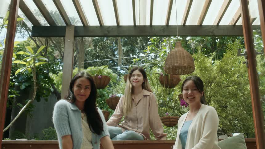 Three women sitting outside under a pergola smiling and posing for the camera