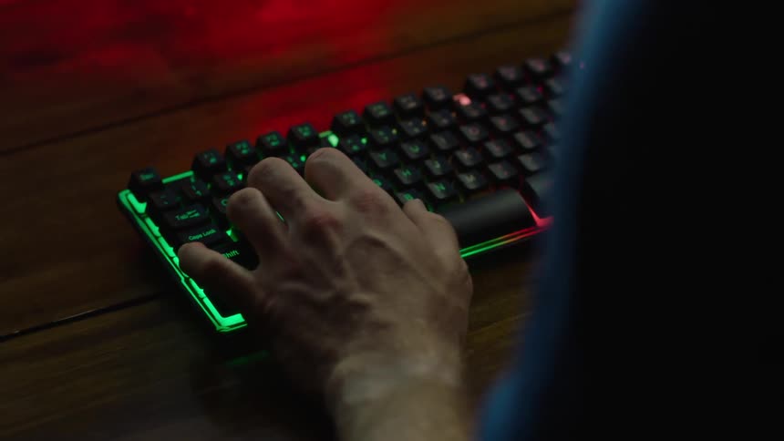Close up of the hands of a man playing video games on a backlit keyboard