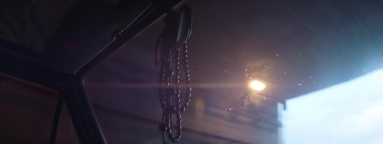The inside of a car is shown through the windshield as it drives under a tunnel with lights and comes out into the daylight