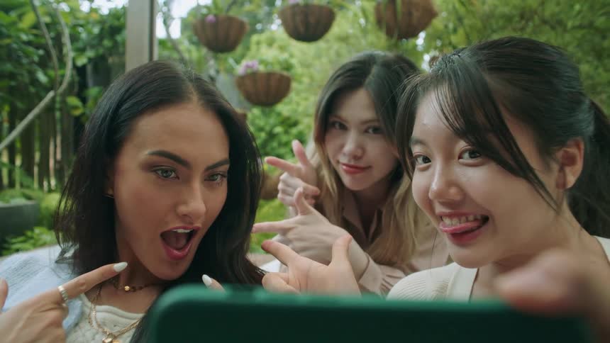 Three women posing pointing and smiling while looking at the one womans camera phone