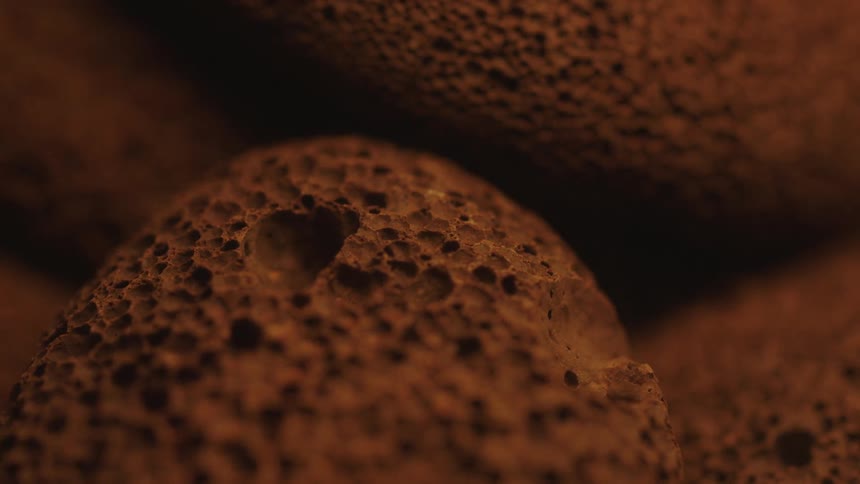 Extreme close up of dust flowing from and around small brown sponge like pebbles