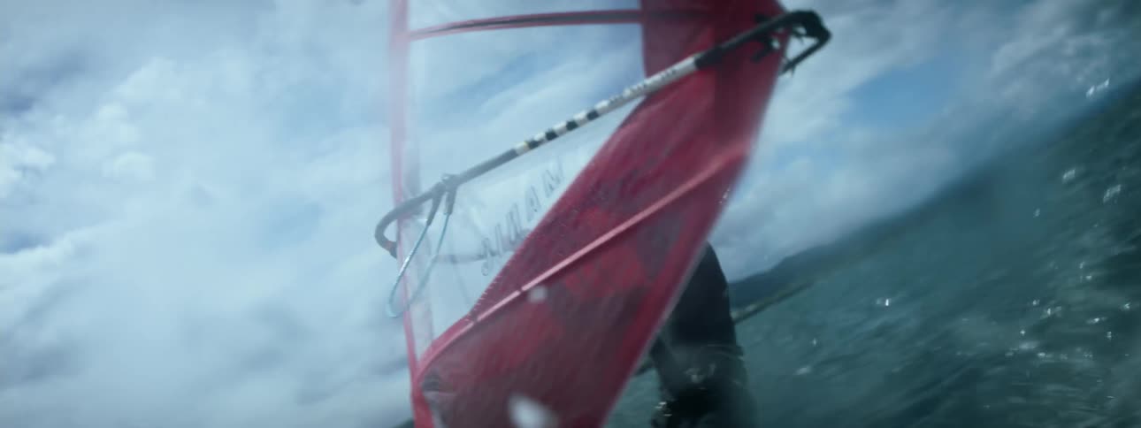 A man sailing on a red wind sail on the ocean with mountains in the distance