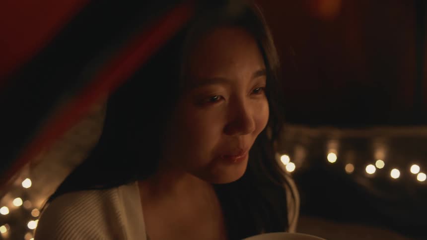 A close up of a womans face as she laughs and smiles while eating out of a bowl