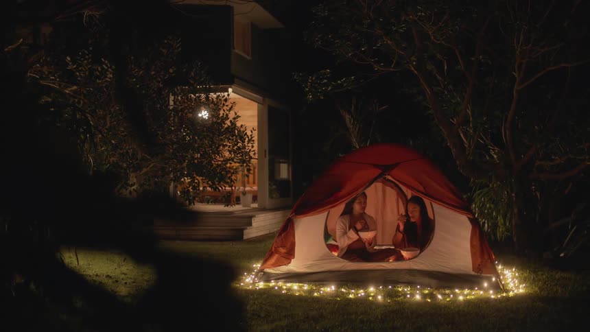 Two friends sitting inside a tent in the backyard surrounded by christmas lights at night