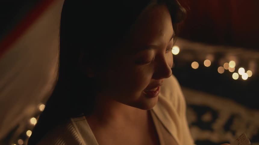 Close up of a girl surrounded by candles on a dimly lit room opening her eyes