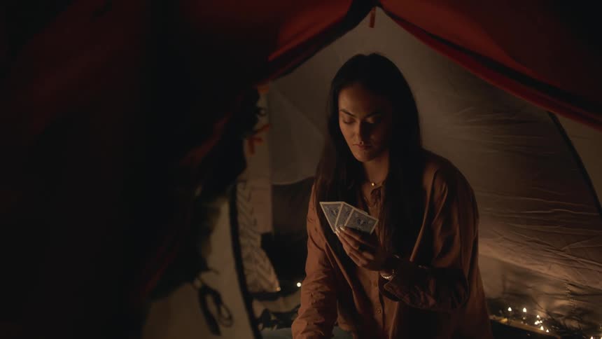 A young woman is sitting inside of a tent and is playing with cards