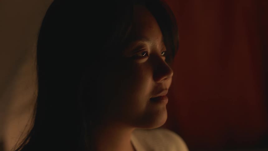 Woman with straight hair and white shirt smiles slightly in the tent at night
