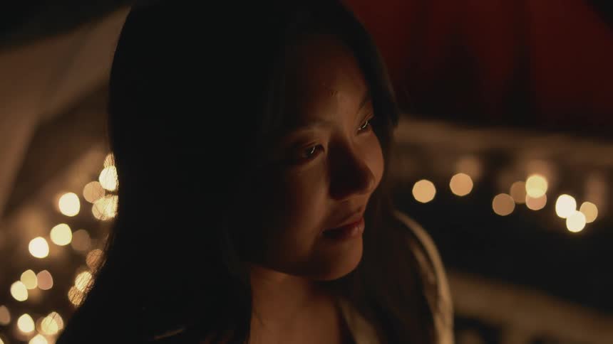 Young woman sitting in a tent at nighttime engaging with a friend listening