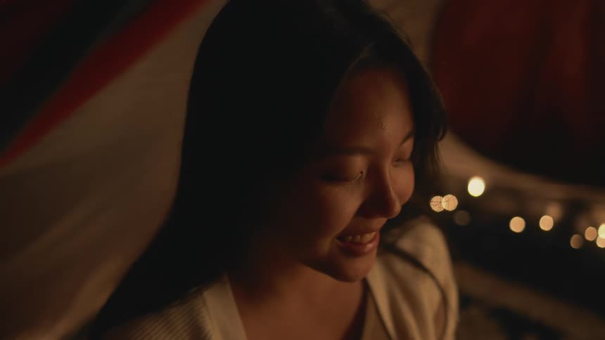 A young asian woman smiles and laughs to herself at night while looking at something