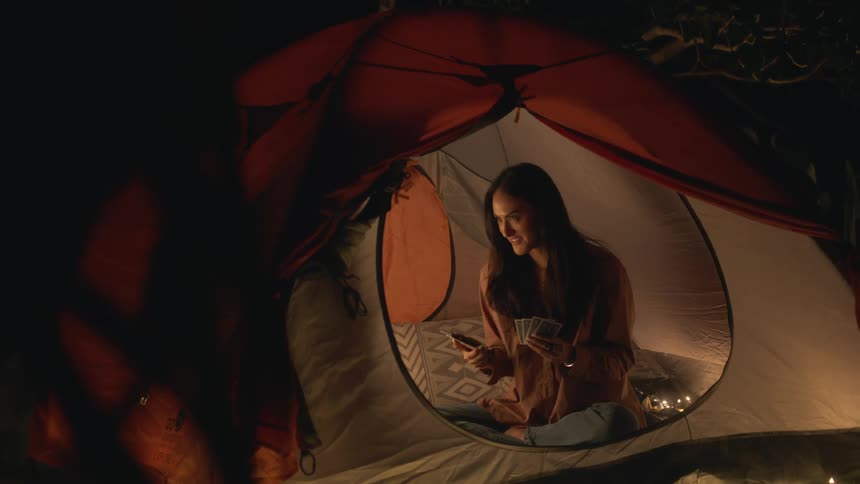 Young woman playing cards inside of a tent in the backyard excitedly picks up the phone