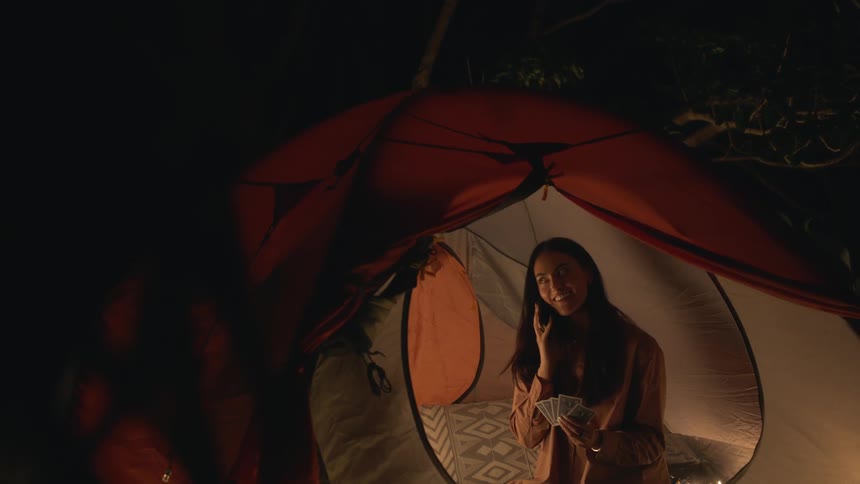 A woman is texting and sitting inside of a tent