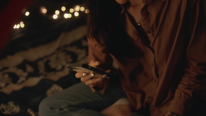 A woman is sitting in a tent and texting on her phone