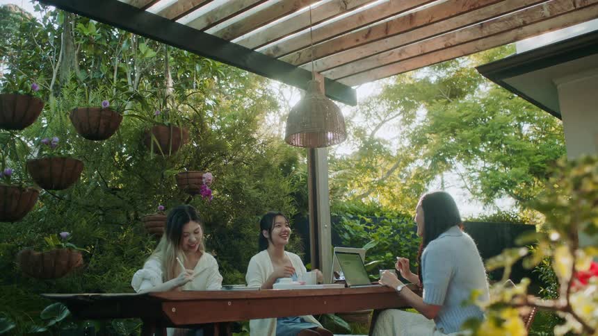 A group of three young women sit together at a table while smiling and talking
