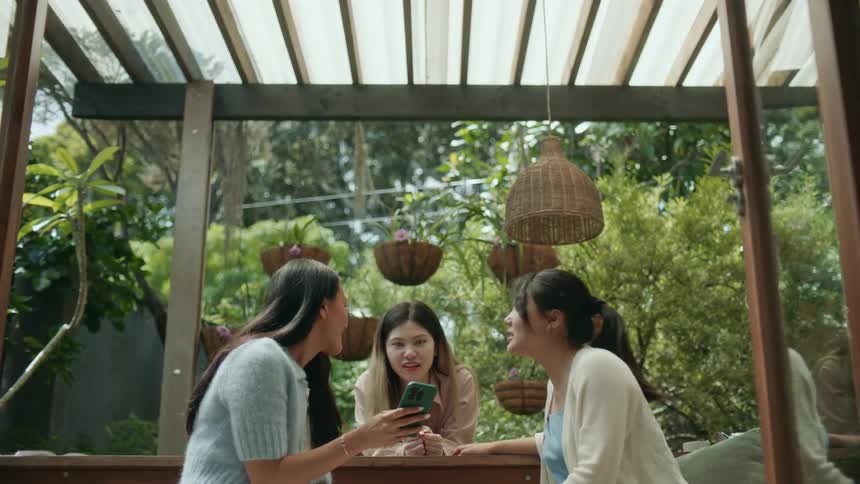 A group of women talk while looking at the screen of a smartphone together as they sit outdoors