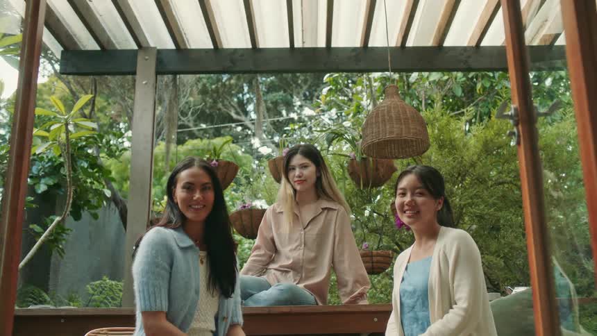 Three young women are smiling and sitting outdoors on a covered patio