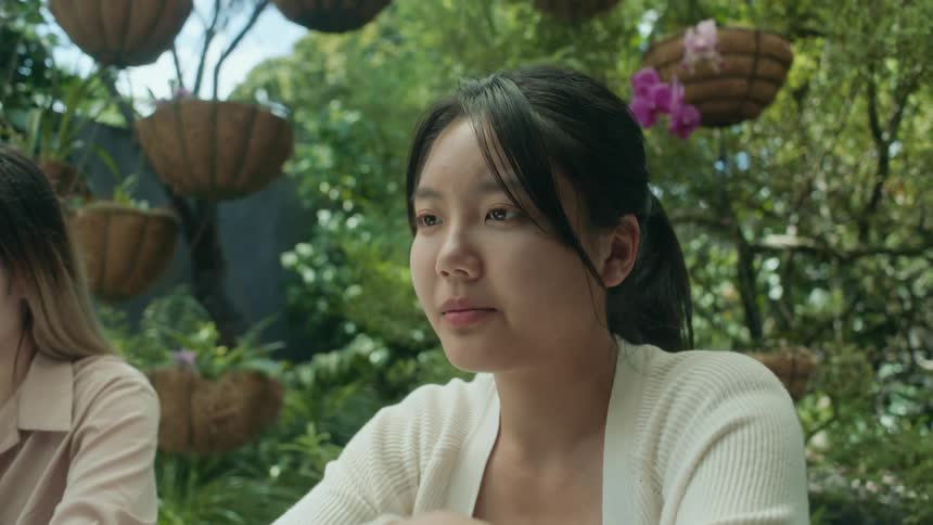 Young bored woman sitting at a table in the garden sighs while listening to her friends