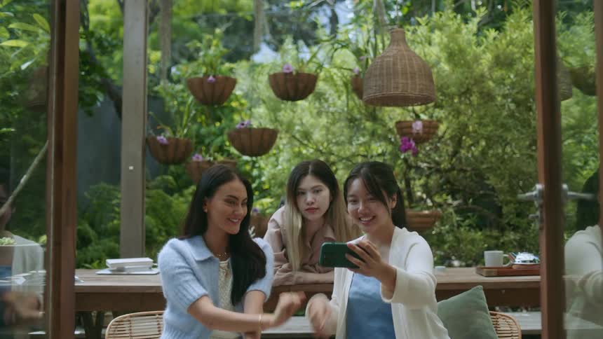 Three women sit outside posing and smiling for a picture on one of the womens phones