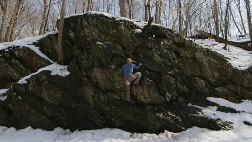 A man climbs rocks in a snowy forest
