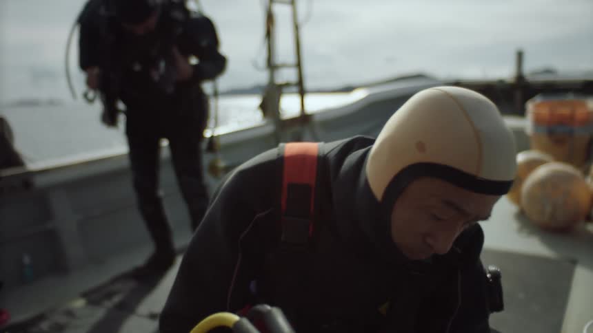 A man kneeling down on a boat adjusting a tank to scuba dive