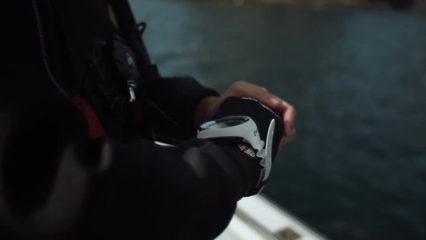 A male diver stands on a boat as it is in motion and he checks his equipment