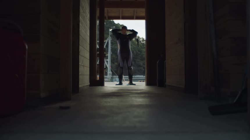 A mans silhouette in a doorway as he puts on a wet suit