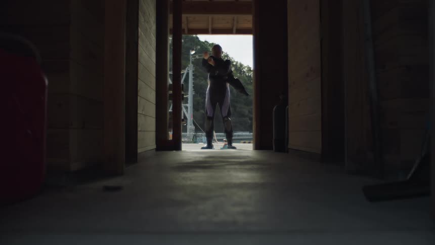 A man standing in a doorway putting on a wet suit
