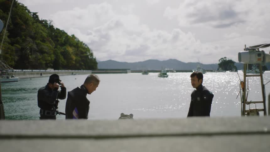 Group of men wearing black wet suits on a boat gearing up for scuba diving