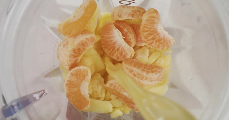 Orange slices and bananas in a blender with orange juice being poured over them