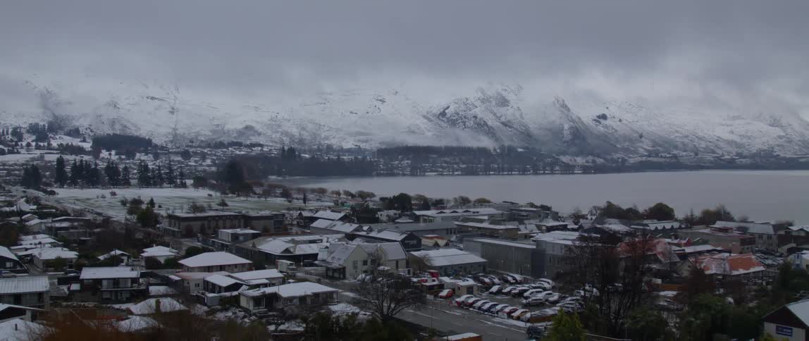A small town is located next to some snow covered mountains and a body of water